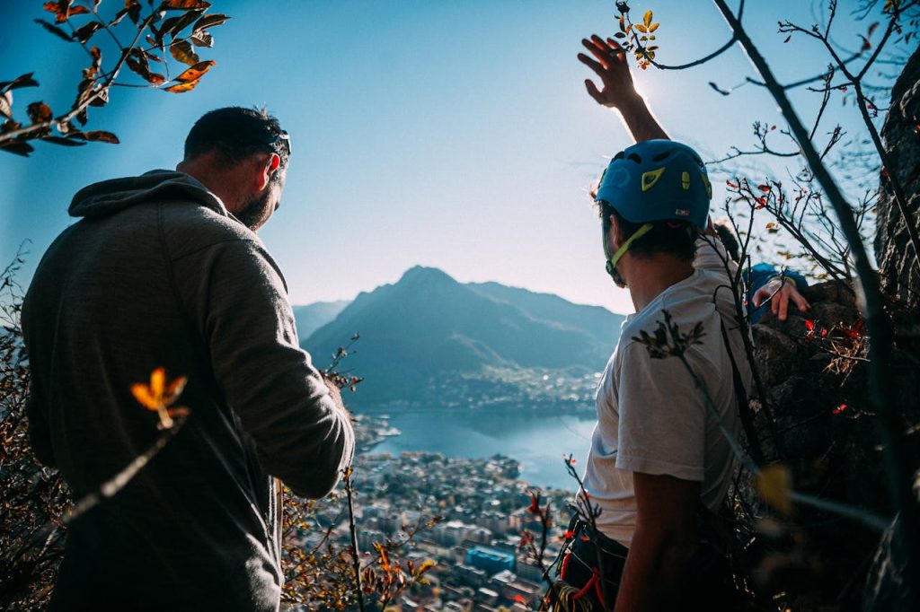 Two men climbing a hilltop overlooking a coastal town with stunning views.